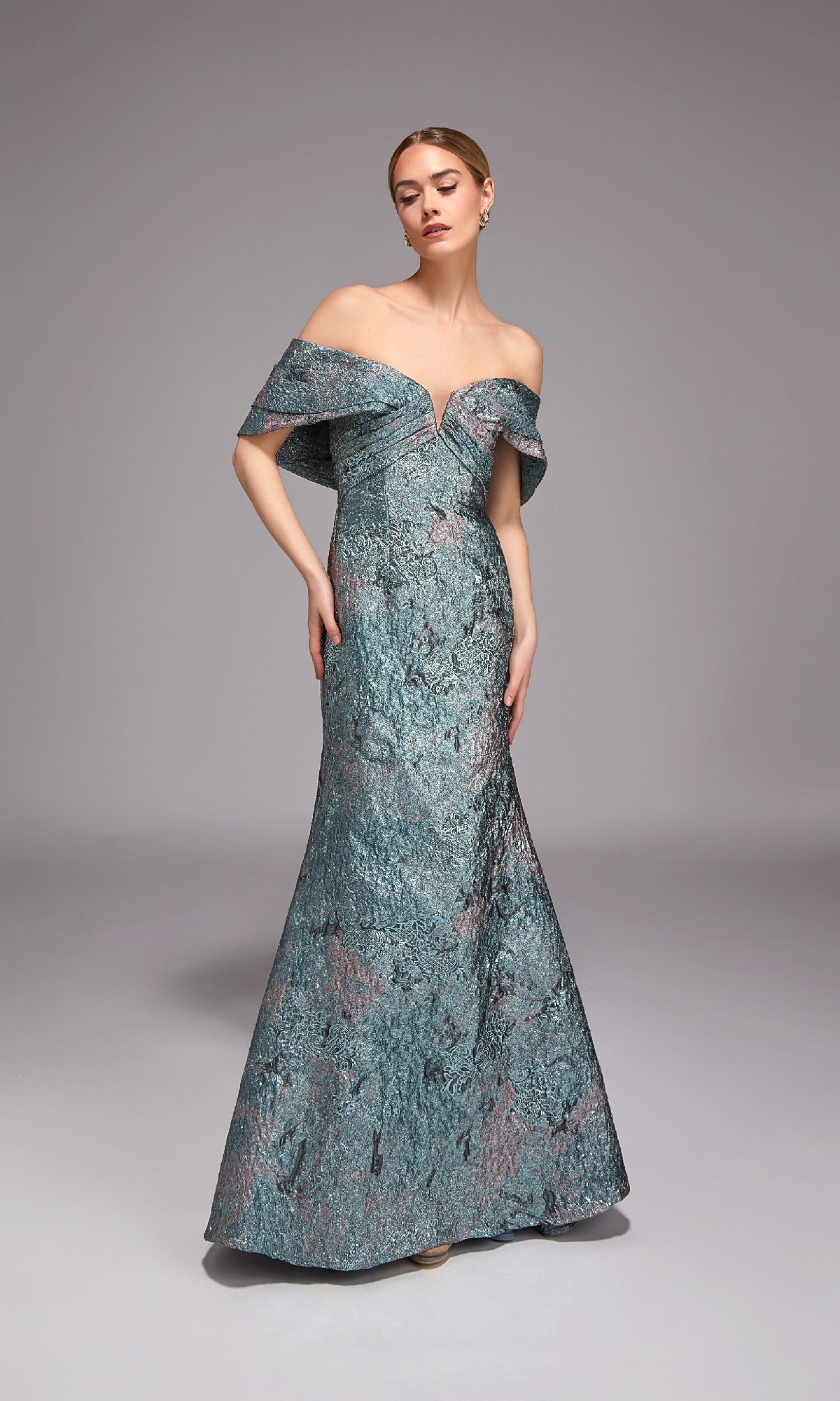 A woman stands against a gray background wearing the Alyce 27794 Long Formal Dress in verdigris, featuring an off-the-shoulder jacquard design with textured fabric and a subtle metallic sheen—ideal for formal occasions.